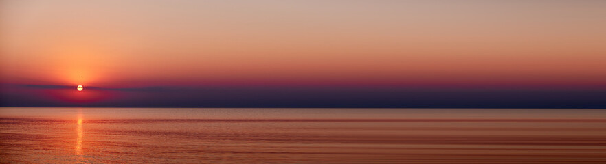 A serene sunset over a calm ocean with birds flying in the sky. Abstract banner of The sun dips...