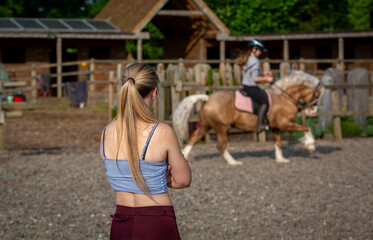 Young girl in her 20's instructing and teaching a horse riding lesson, Image shows a blonde girl on...