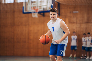 A young basketball kid dribbling a ball on training at indoor court.