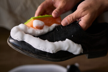 A person is scrubbing a shoe with a sponge and foamy cleaner