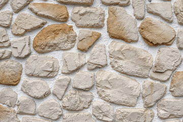 Decorative stone wall made of natural rocks of different colors and shapes plastered with white mortar as a background