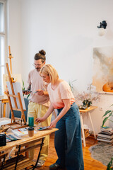 Artistic painter couple standing at atelier and painting on easel together