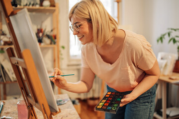 Professional female artist painting on easel at creative art studio.