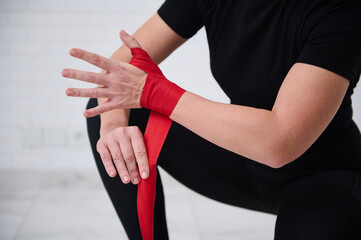 Fototapeta premium Selective focus on hands of female fighter preparing for boxing competition challenge training, tying tapes before putting boxing gloves, isolated over white background. Sport and martial art concept