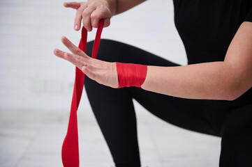 Close-up strong woman boxer fighter preparing boxing bandages, wrapping her wrist and hands with a...