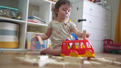 baby plays with a toy bus and puts wooden sticks in the hatch. development of fine motor skills concept. baby learns to put sticks toys into a lifestyle bus car indoors in kindergarten