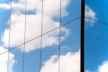 Close-up of glass building facade with blue sky and clouds reflecting in it, abstract background