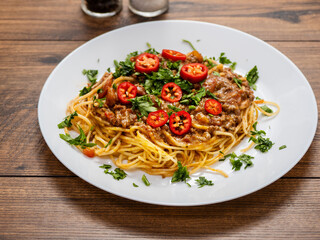 A plate of spaghetti with meat sauce and tomatoes. The plate is on a wooden table. The dish looks delicious and inviting. Italian style meal made with high quality product.