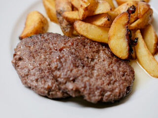 Beef burger and potato wedges on a white plate. Simple plain meal. Dinner with meat product and vegetable.