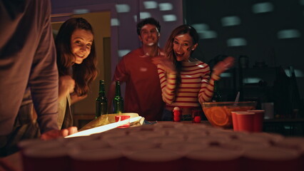 Friends have beer pong competition in disco lights indoors. Mates having fun