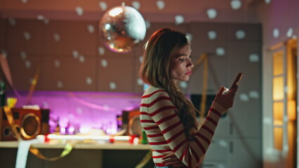 Sad party girl scrolling smartphone under disco ball close up. Woman reading 