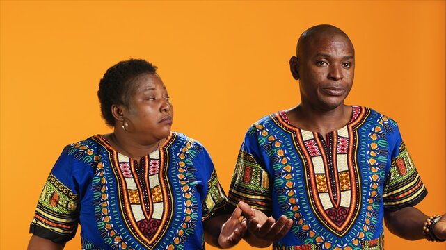 Unsure african american people doing i dont know sign in studio, showing doubtful clueless gesture on camera. Man and woman being uncertain, posing over orange background.