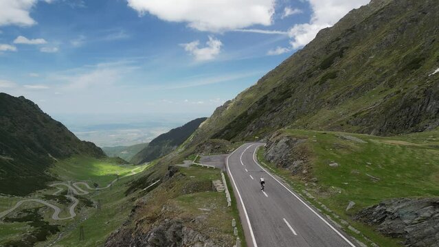 Aerial view of cyclist riding in Carpathian mountains on winding road.  Transfagarasan, Romania. Fit female cyclist is riding bicycle between mountain hills. Pedaling through nature. Transylvania