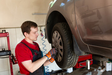 a mechanic stands by a car in a car service center. master removes a wheel from a car, repair, wheel replacement
