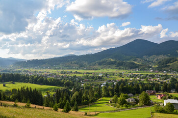 Naklejka premium Rural landscape is adorned with scattered houses, verdant trees, and majestic mountains with patches of forests in the background. Verkhovyna, Carpathian Mountains, Ukraine