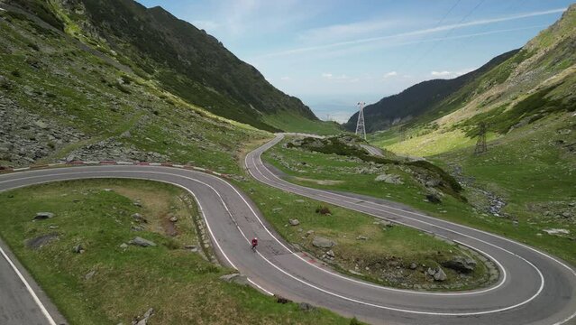 An aerial drone shot captures a female cyclist riding a bicycle on an asphalt road in the mountains, offering an amazing view. Cycling on the serpentine Transfagarasan road. Sport motivation. 