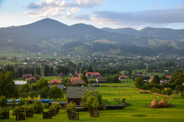 Rural landscape is adorned with scattered houses, verdant trees, and majestic mountains with patches of forests in the background. Verkhovyna, Carpathian Mountains, Ukraine
