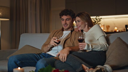 Loving newlyweds spending evening date on cozy couch holding wine glasses.