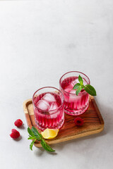 Raspberry cocktail with ice in a glass on a light background