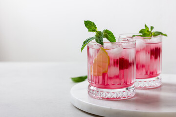 Raspberry cocktail with ice in a glass on a light background