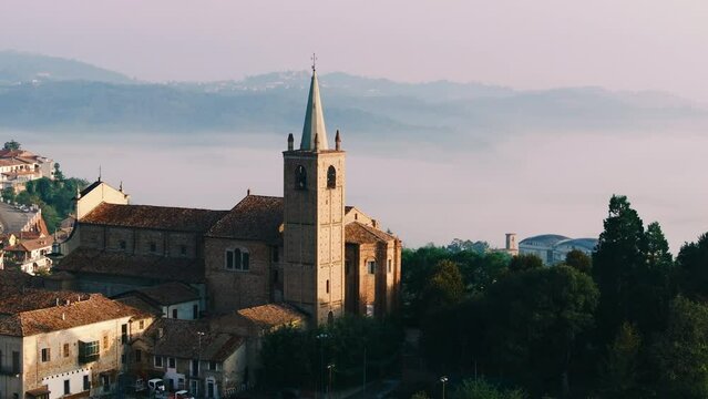 Moncalvo, Piedmont, Italy 10 11 2023: Chiesa di San Francesco medieval church on a Italian hill with a town in the background and scenic hills covered with mist during sunrise in the province of Asti