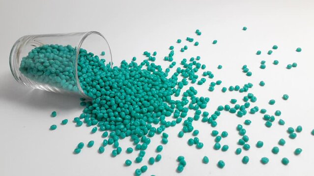 Turquoise masterbatch granules spill from the shot glass, this polymer is a coloring product for products in the plastics industry