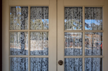 A pair of wooden doors with glass windows and a white lace curtain, featuring old-fashioned style home decor, classic vintage, and nostalgia vibe.