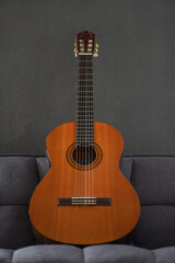 Creole guitar standing on top of a gray sofa with a grey wall on background