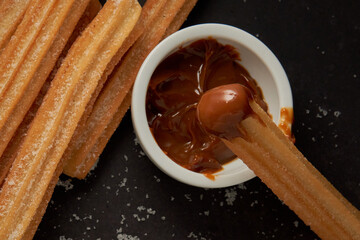 Churro with dulce de leche on the tip and more churros on a black background