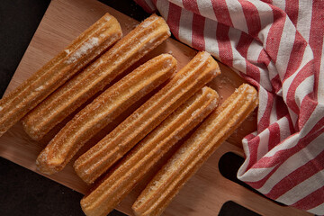 Homemade Churros argentine with sugar on a wooden board and a cloth napkin, black background. top view