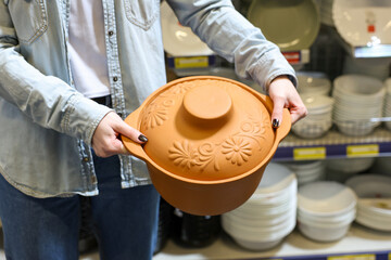 A woman is holding a clay pan or pot with a floral design on it