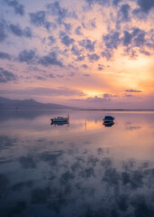 Fototapeta premium boats waiting in the reflective water clouds in the sky sunset colors