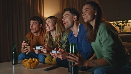 Gambling people playing video game on living room couch at night close up. 