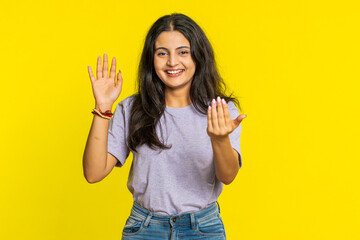 Young Indian woman smiling friendly at camera, waving hands gesturing hello greeting or goodbye...