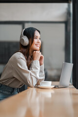 Obraz premium A woman wearing headphones is sitting at a table with a laptop and a cup of coffee. She is smiling and she is enjoying her time