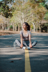 A woman is sitting on the side of a road with a bottle of water in her hand. She is wearing a grey shirt and grey pants