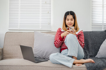A woman is sitting on a couch with a laptop and a cell phone in her hands. Concept of multitasking...