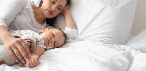 Adorable baby sleeping with toy and mother on bed
