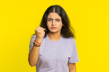 Fototapeta premium Aggressive angry Indian young woman trying to fight at camera, shaking fist, boxing with expression, punishment, threaten, bullying, abuse, mad fury. Arabian girl isolated on yellow studio background