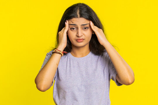 Displeased exhausted Indian Hindu woman girl rubbing temples to cure headache problem, suffering from tension, migraine, stress, grimacing in pain, high blood pressure isolated on yellow background