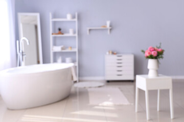 Blurred interior of modern bathroom with beautiful pink dahlias in vase on table