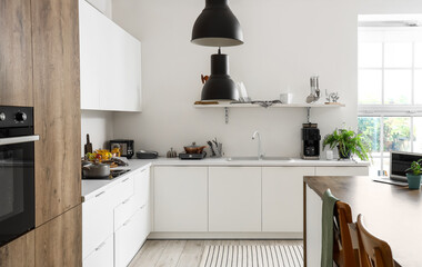 Fototapeta premium Interior of modern kitchen with white furniture and wooden island table