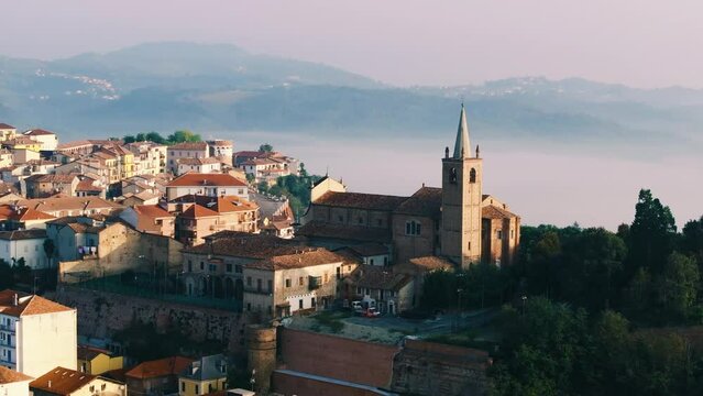 Moncalvo, Piedmont, Italy 10 11 2023: Chiesa di San Francesco medieval church on a Italian hill with a town in the background and scenic hills covered with mist during sunrise in the province of Asti