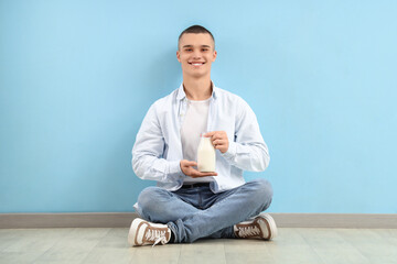 Teenage boy with bottle of milk sitting near blue wall