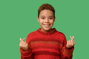 Cute little African-American boy showing heart gesture on green background. Valentine's day celebration