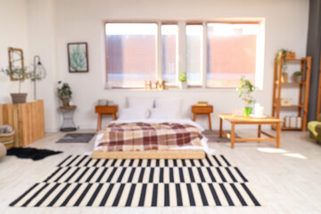 Blurred view of light bedroom with bed, tables and window