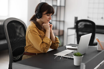 Woman in headphones watching webinar at table in office