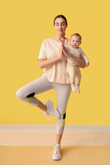 Beautiful young sporty woman with her little baby meditating near yellow wall