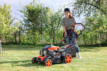 Smiling woman cutting green grass with lawn mower in garden