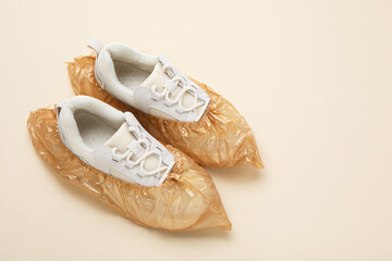 Sneakers in shoe covers on beige background, above view. Space for text
